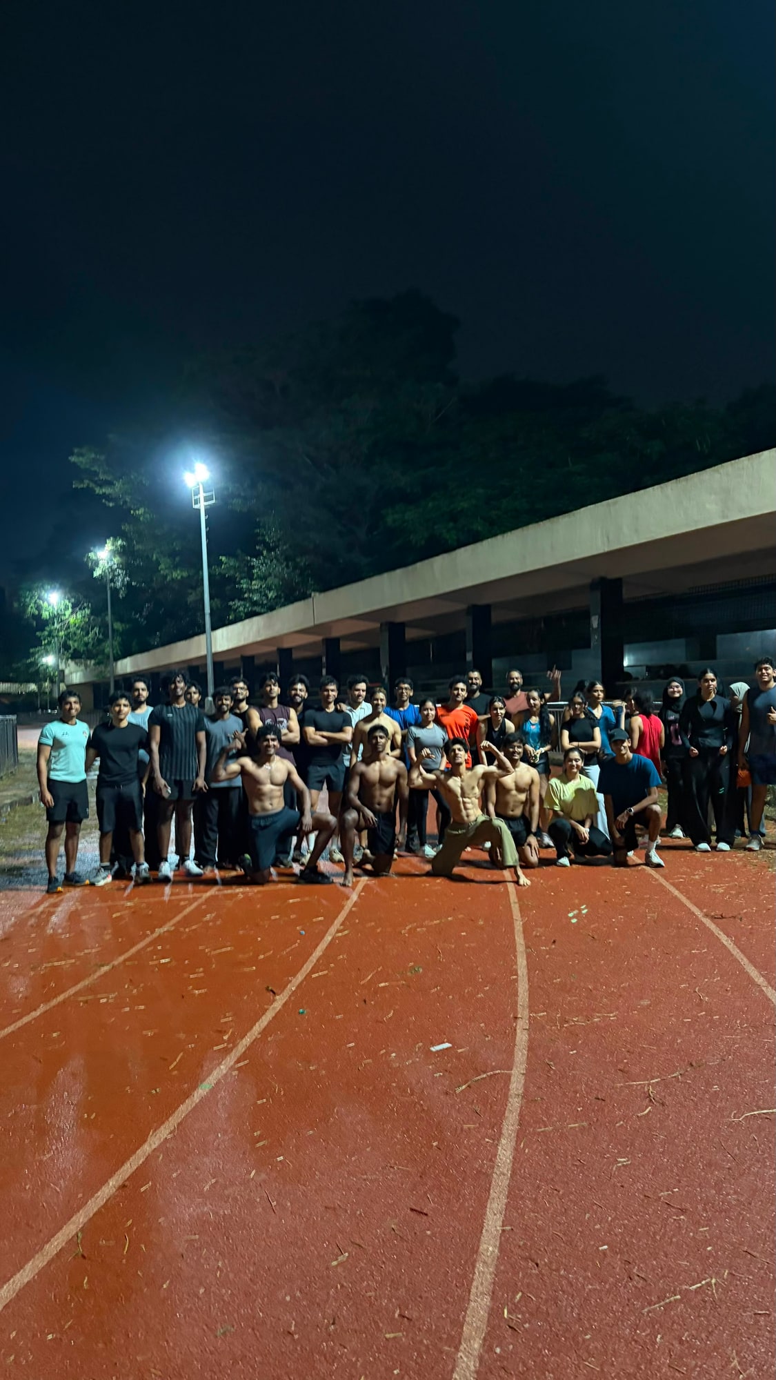 A group of runners posing on a floodlit running track at night after an interval session