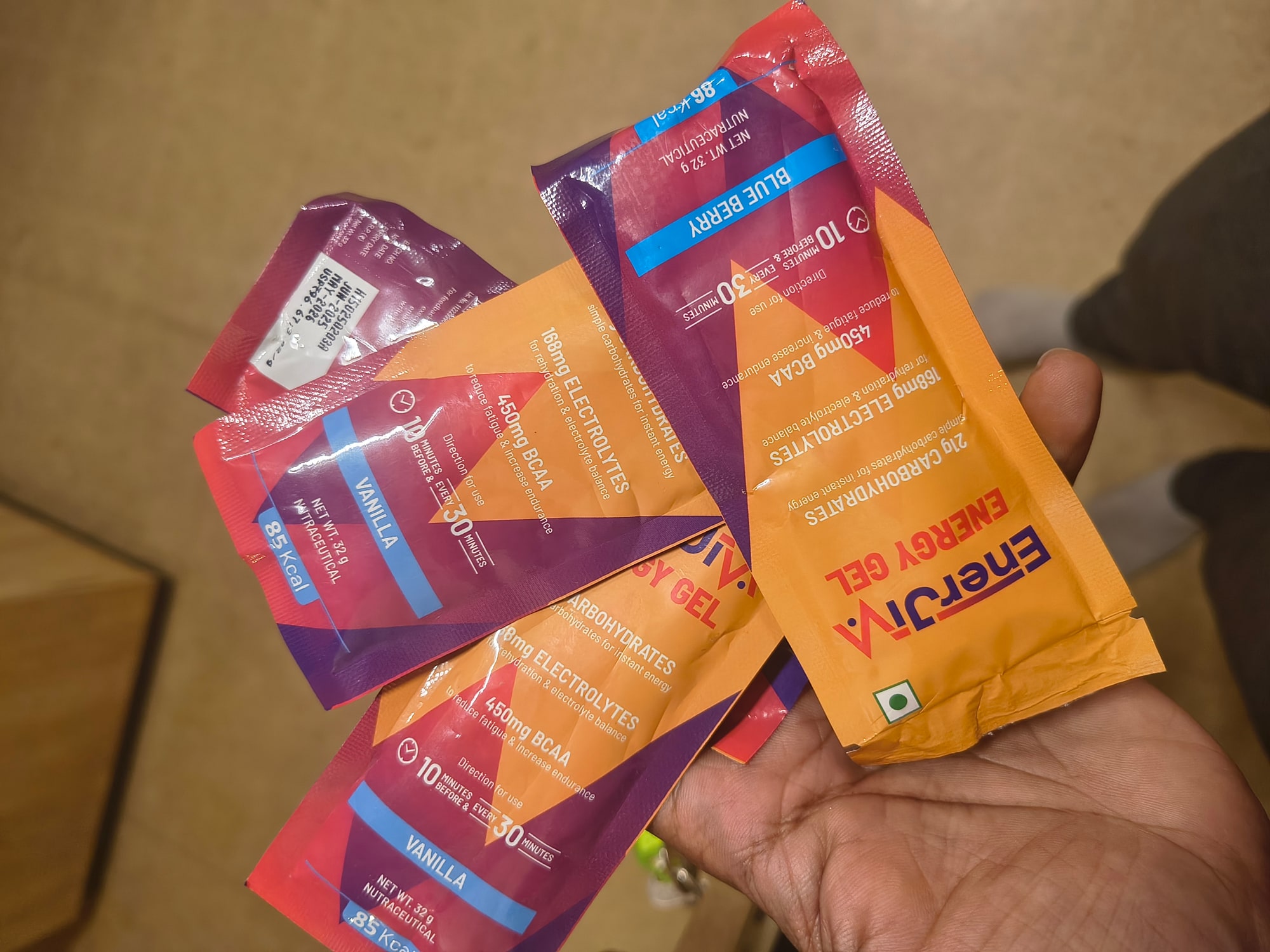 A hand holding four vanilla and blueberry energy gel sachets from the race kit