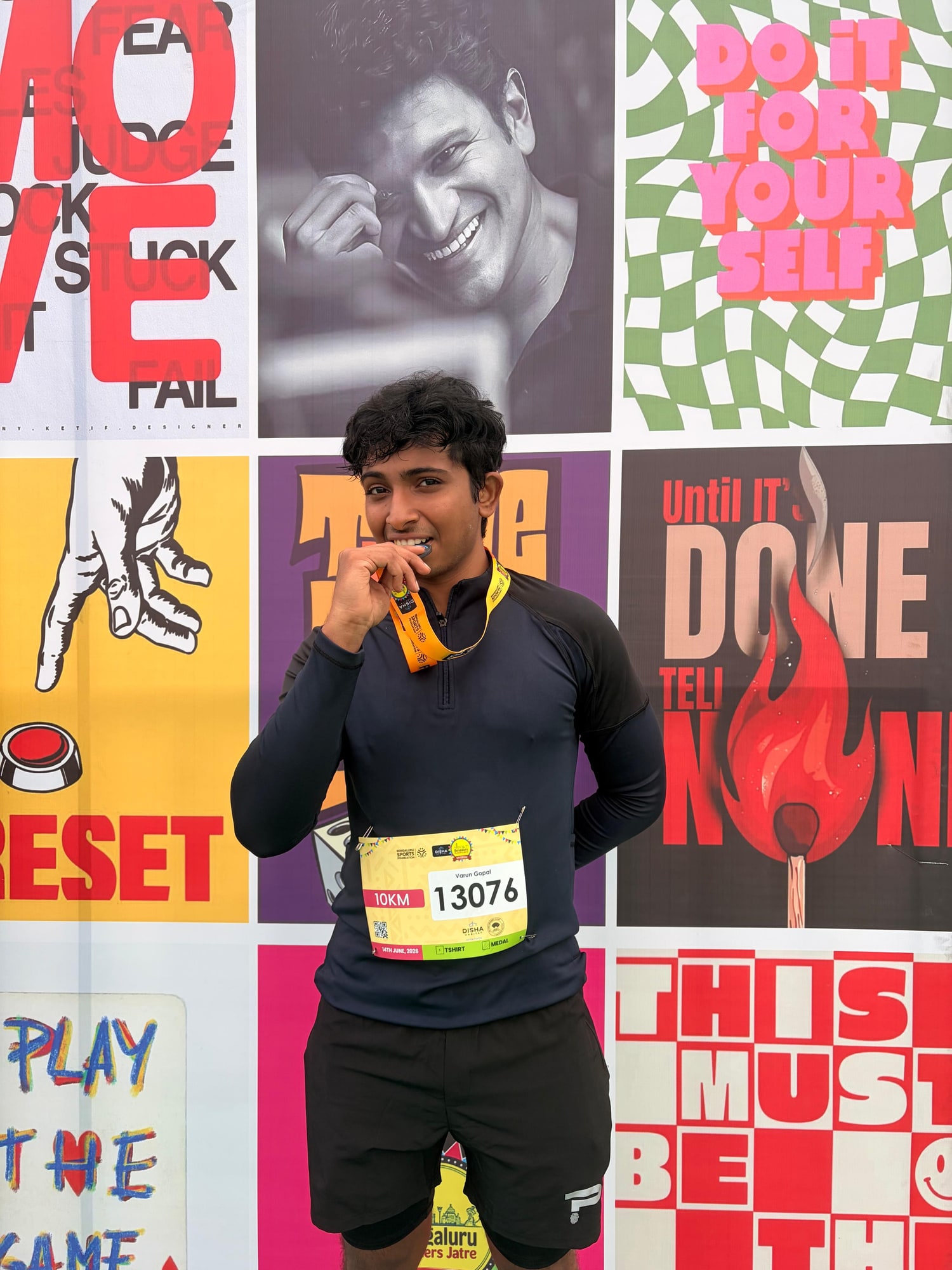 A finisher biting his medal in front of a wall of brightly coloured motivational posters