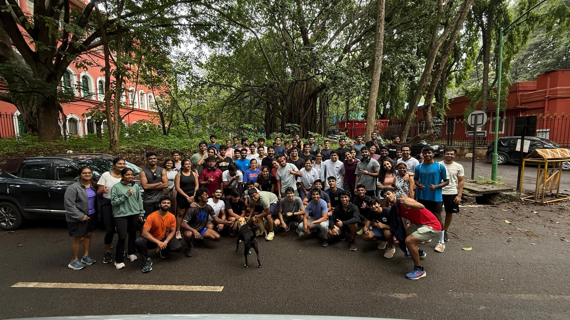 A group of around sixty runners posing together on a tree-lined road beside Cubbon Park after a morning run