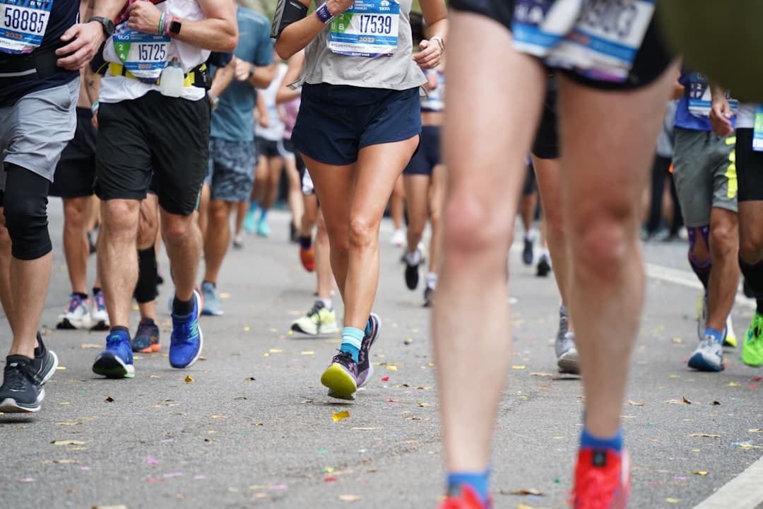 Runners' legs mid-race on a road scattered with confetti, race bibs pinned on