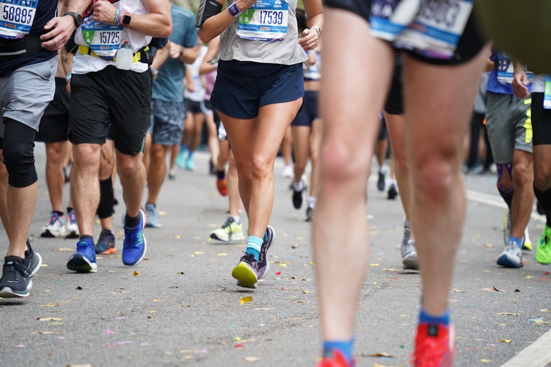 Runners' legs mid-race on a road scattered with confetti, race bibs pinned on