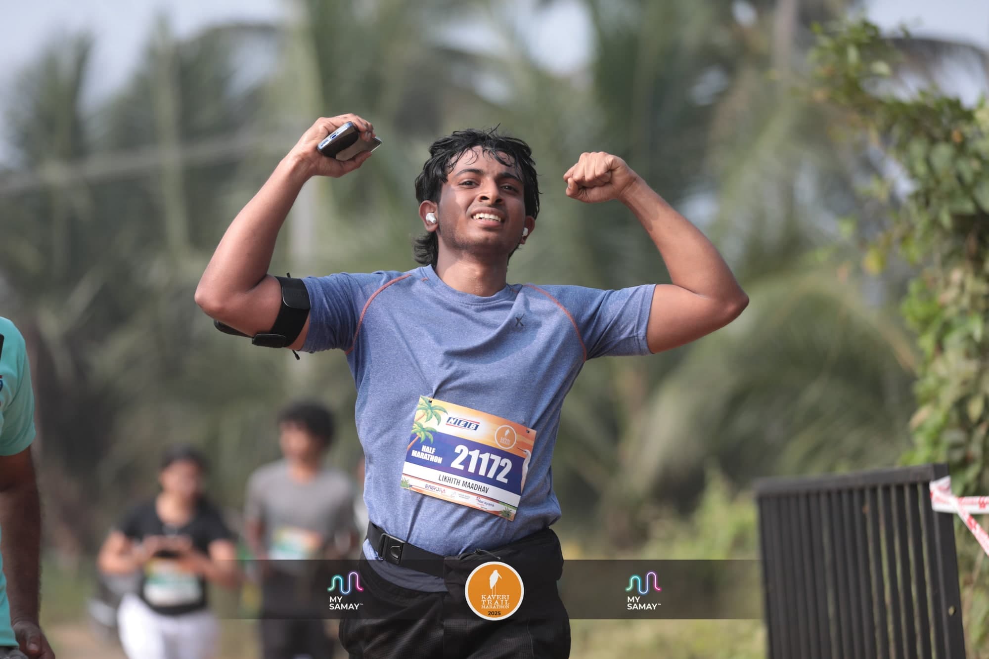 A half marathon runner flexing both arms as he comes down the finish chute at the Kaveri Trail Marathon